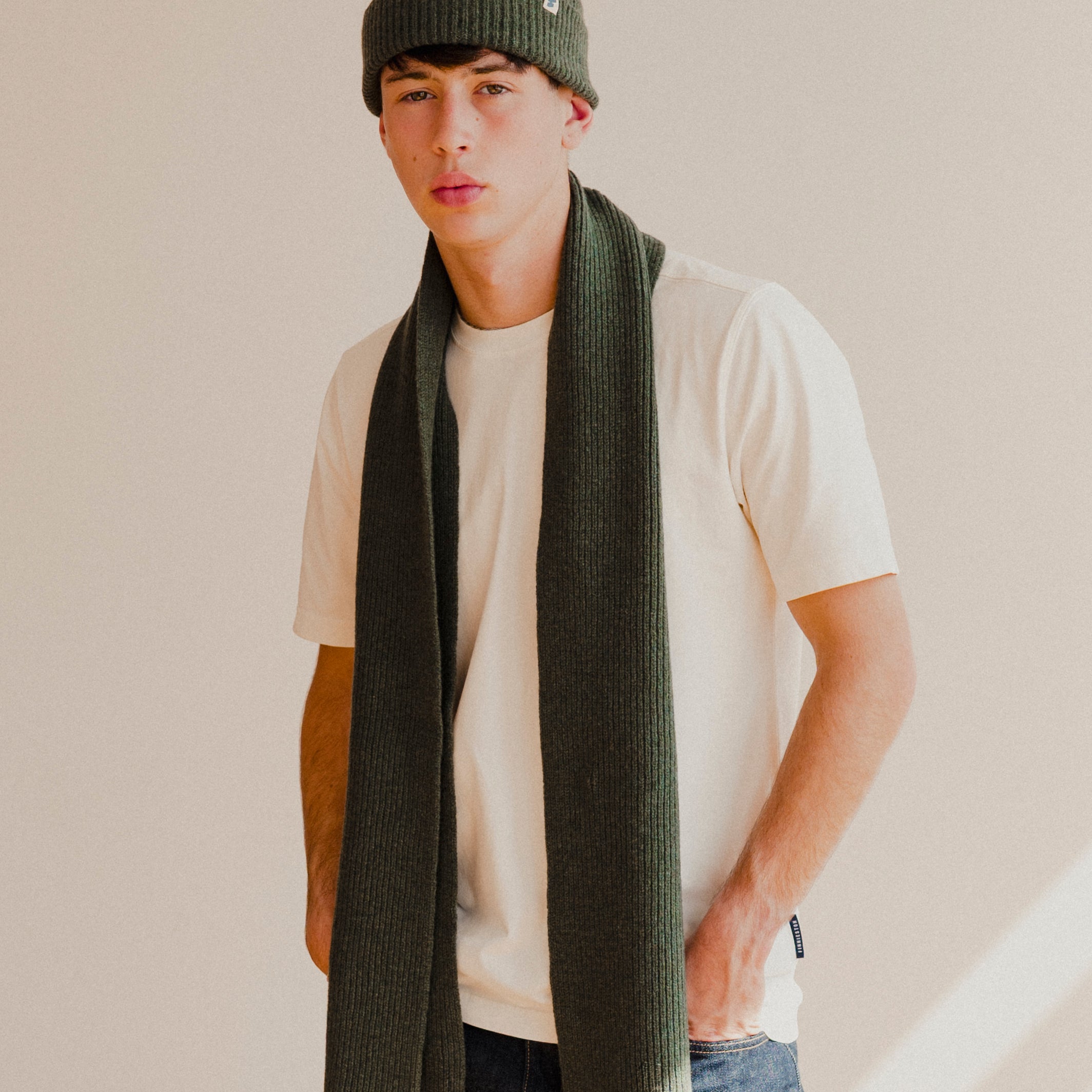 Person wearing a green beanie plain white t-shirt and scarf with a plain background