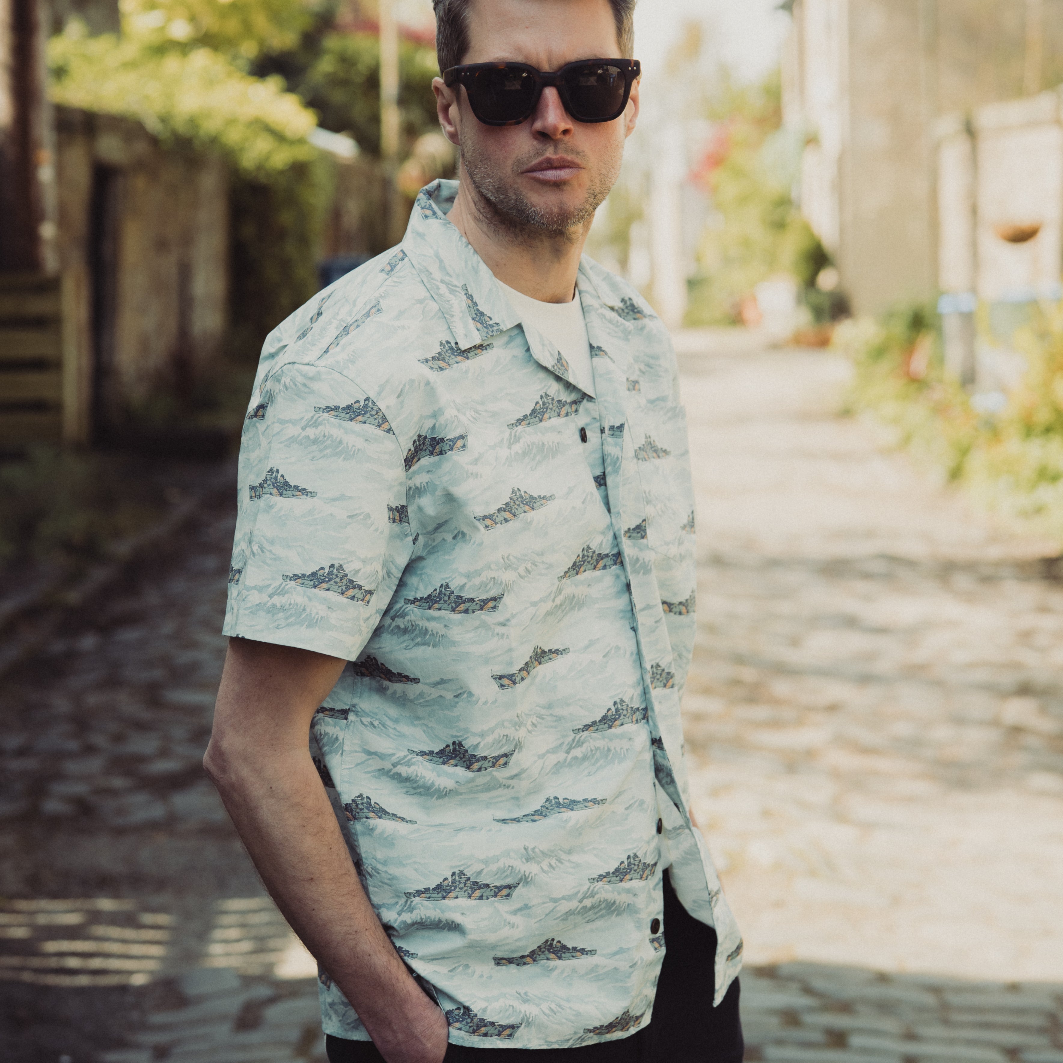 Man wearing a light-colored patterned shirt and sunglasses outdoors.