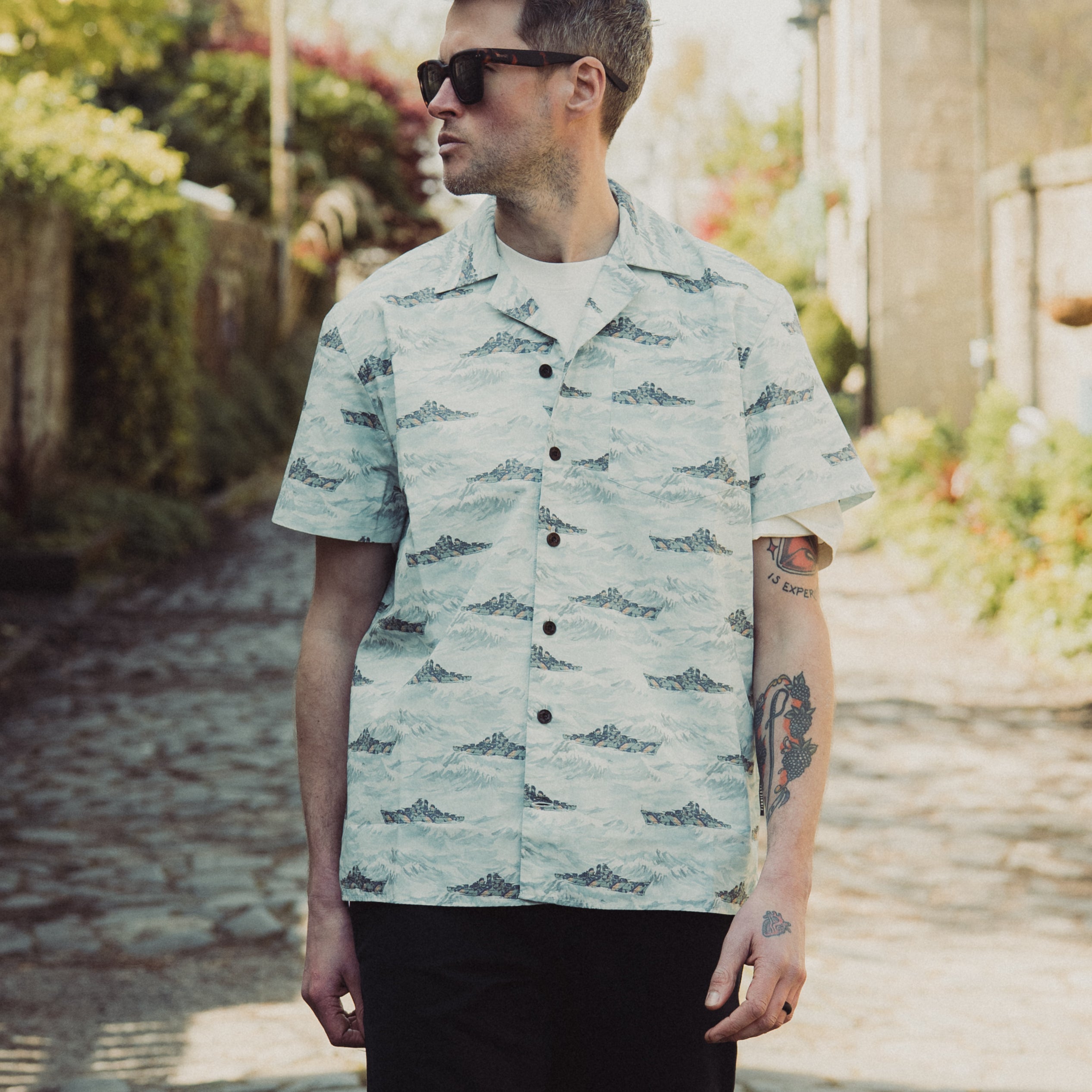 Man wearing a light green patterned shirt standing outdoors on a sunny day.