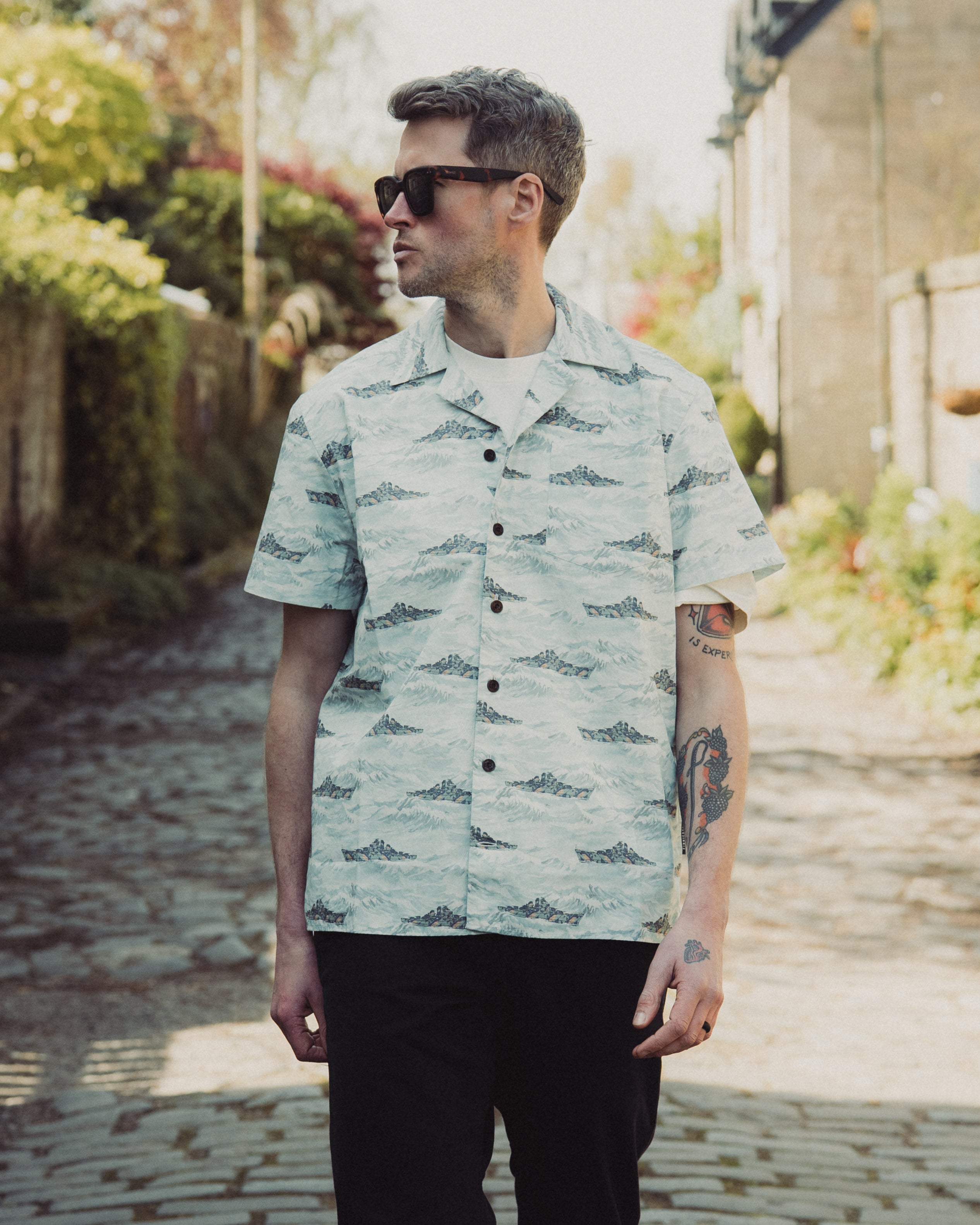 Man wearing a light green patterned shirt standing outdoors on a sunny day.