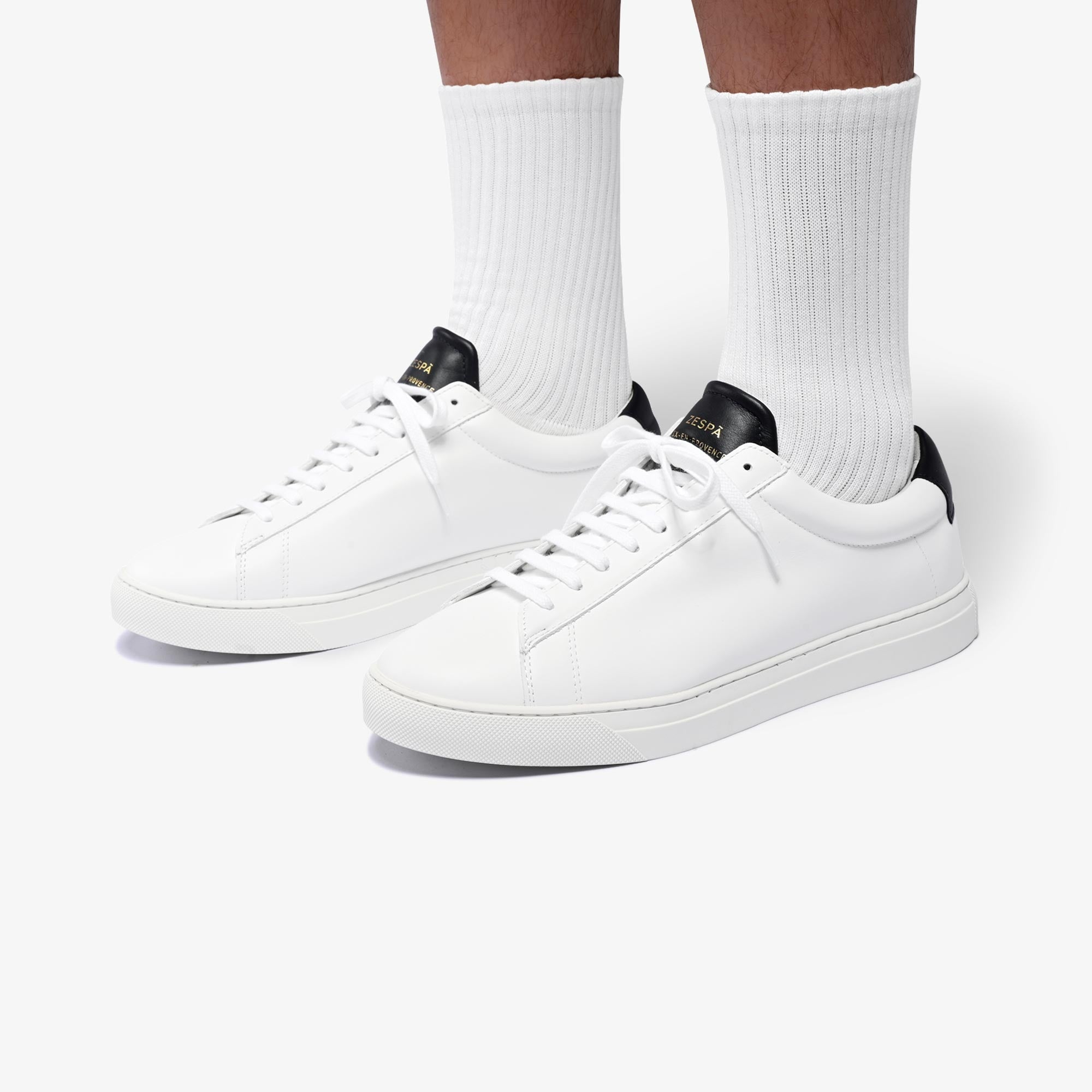 White sneakers worn with white socks on a light gray background