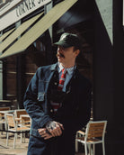 Man in a denim jacket and cap standing in front of a building with an awning.