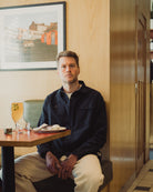 Man sitting at a table in a restaurant with a painting on the wall behind him.