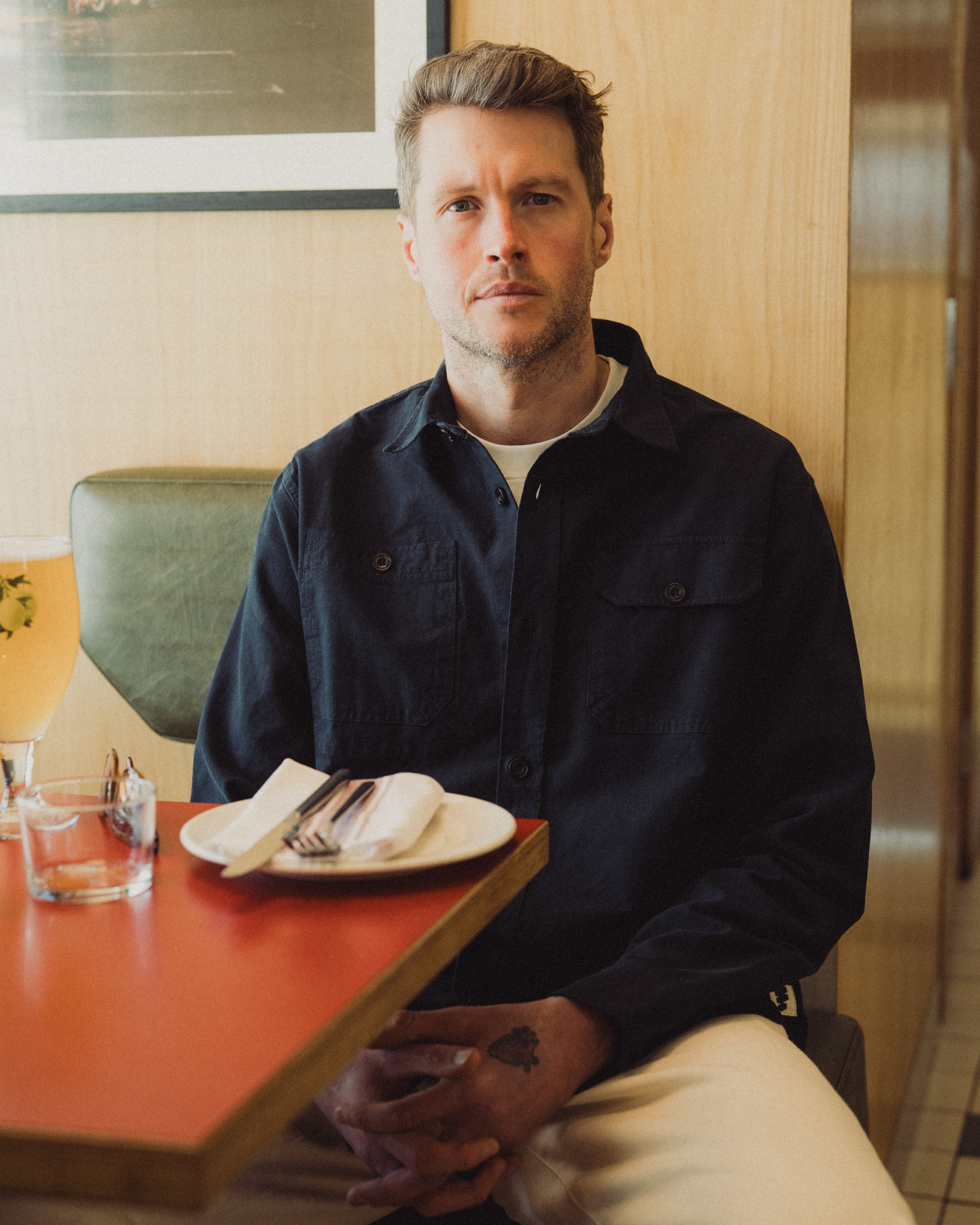 Man sitting at a table in a casual setting with a plate of food and a drink.