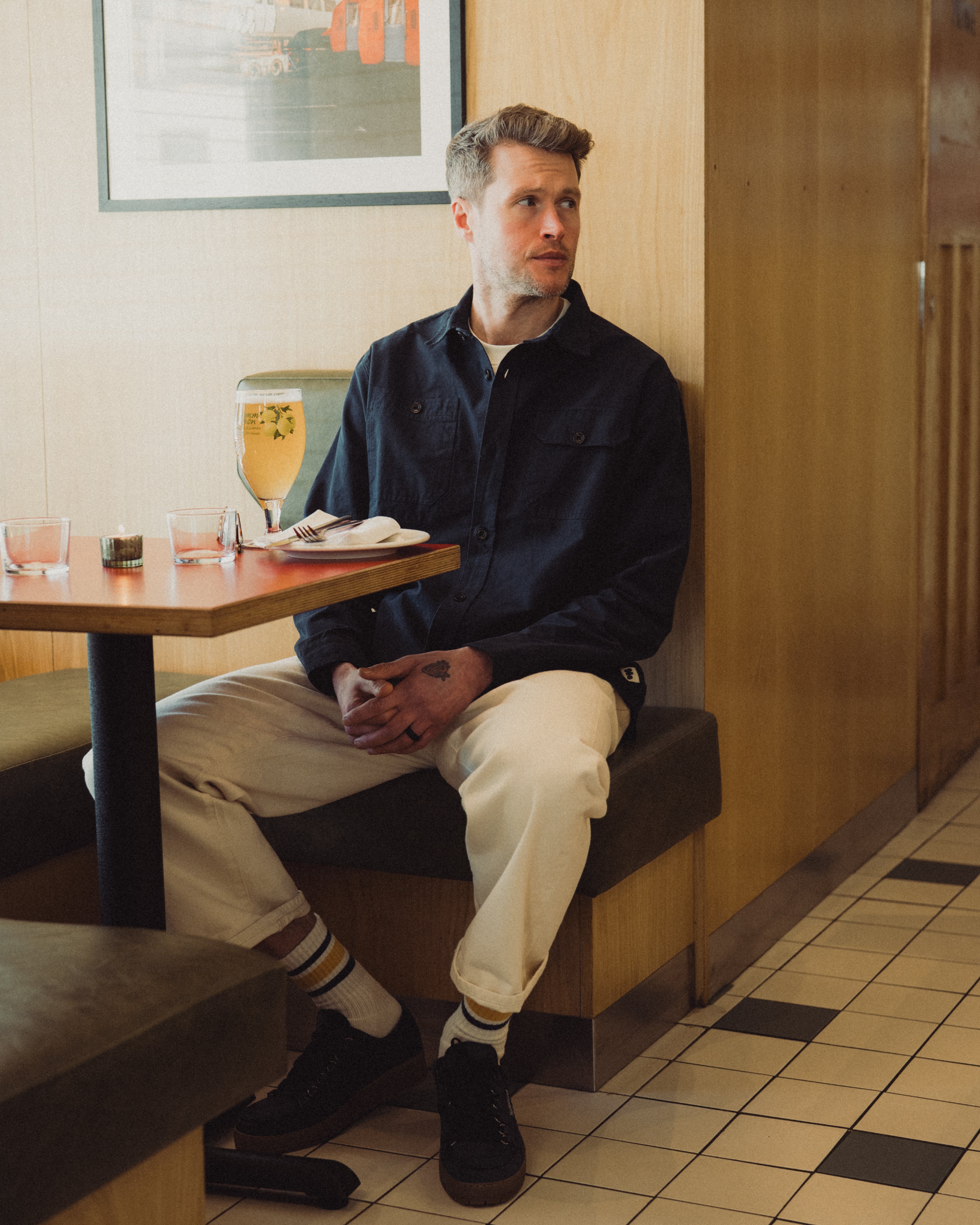 Man sitting alone in a diner booth with a drink and napkin on the table.