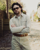 Man wearing sunglasses and a light-colored shirt with a blurred outdoor background
