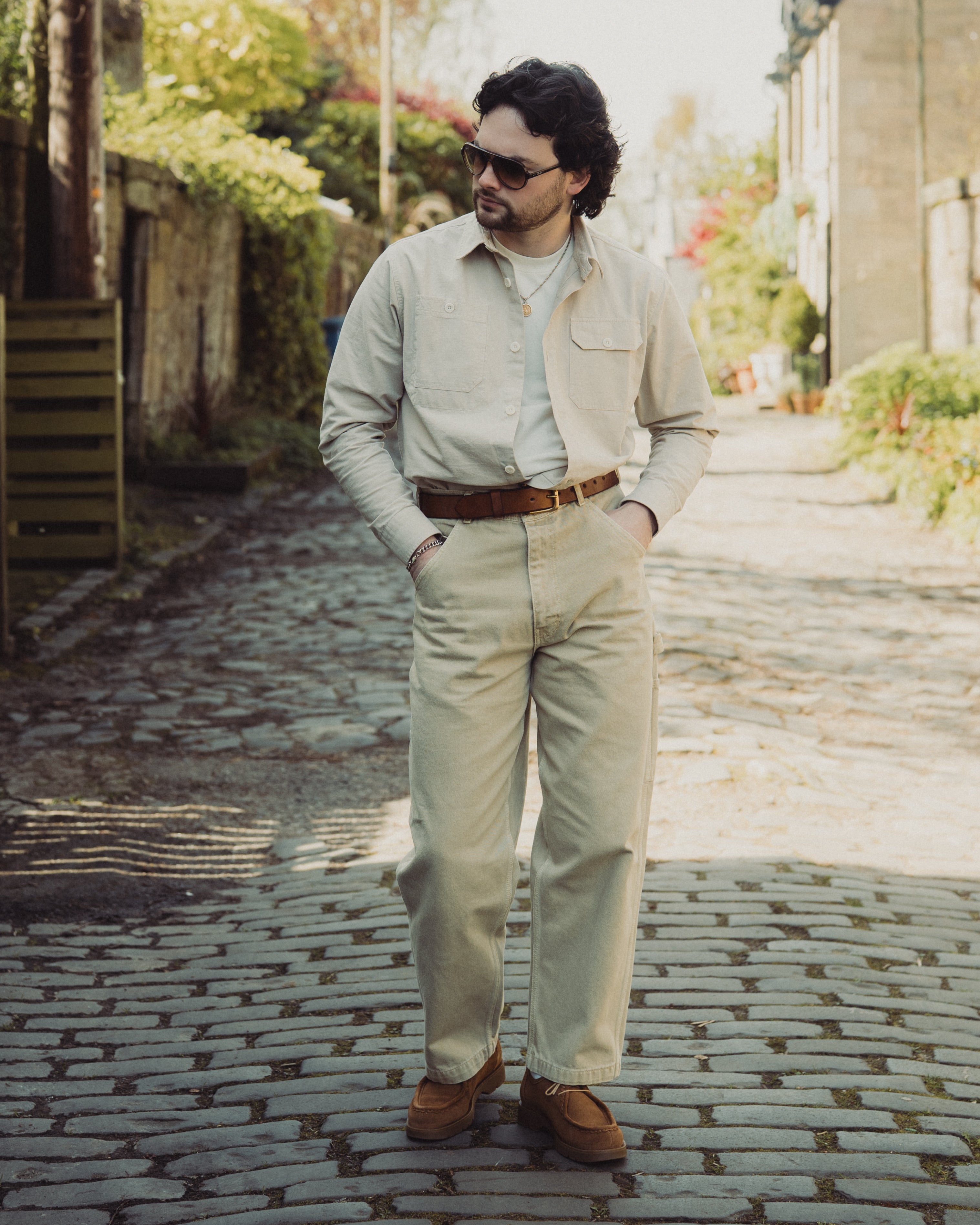 Man in beige suit and sunglasses standing on a cobblestone street.