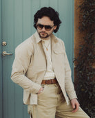Man wearing sunglasses and a beige outfit in front of a green door.