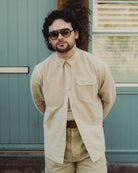Man wearing sunglasses and a beige shirt standing in front of a teal door.