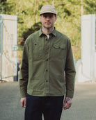 Man wearing a green jacket and beige cap standing outdoors with blurred background