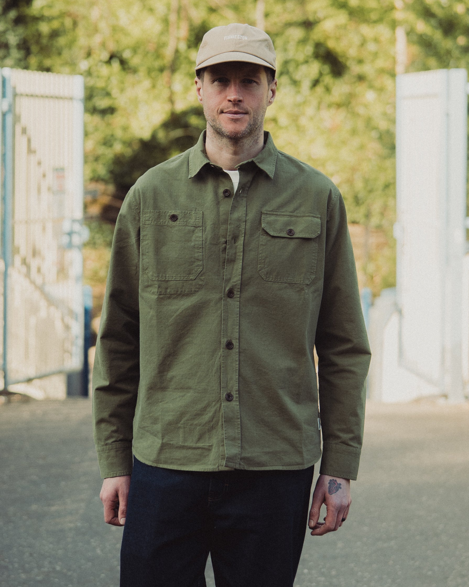 Man wearing a green jacket and beige cap standing outdoors with blurred background