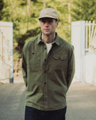 Man wearing a green jacket and beige cap standing outdoors with blurred background