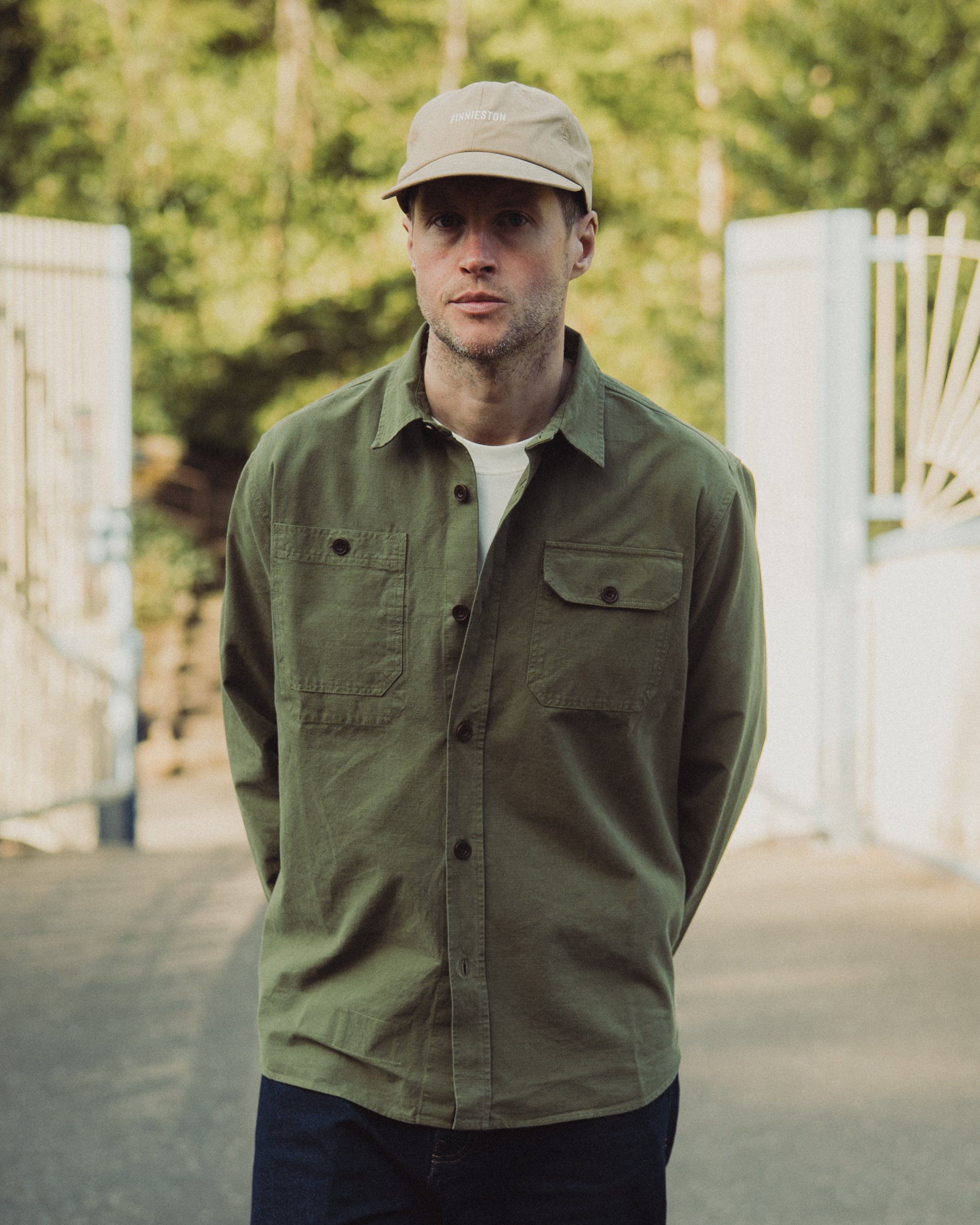 Man wearing a green jacket and beige cap standing outdoors with blurred background