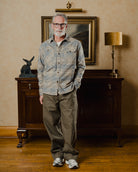 Man standing in a room with a painting and lamp in the background