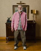 Man wearing a pink cardigan in a room with wooden furniture and a lamp.