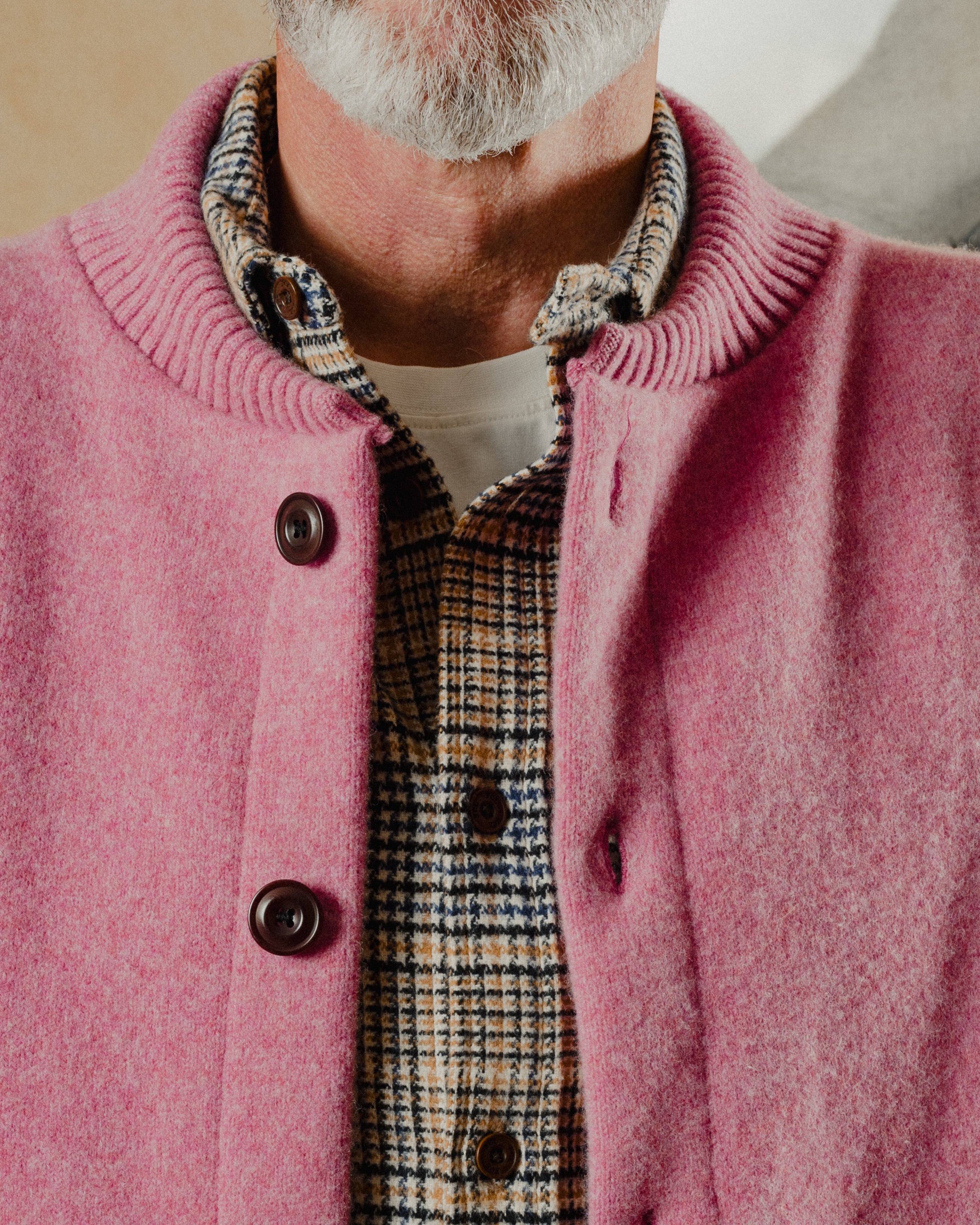Close-up of a person wearing a pink cardigan over a plaid shirt.