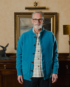 Man wearing a blue cardigan in a room with a painting and lamp in the background