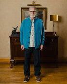 Man wearing a blue cardigan in a room with wooden furniture and a lamp.