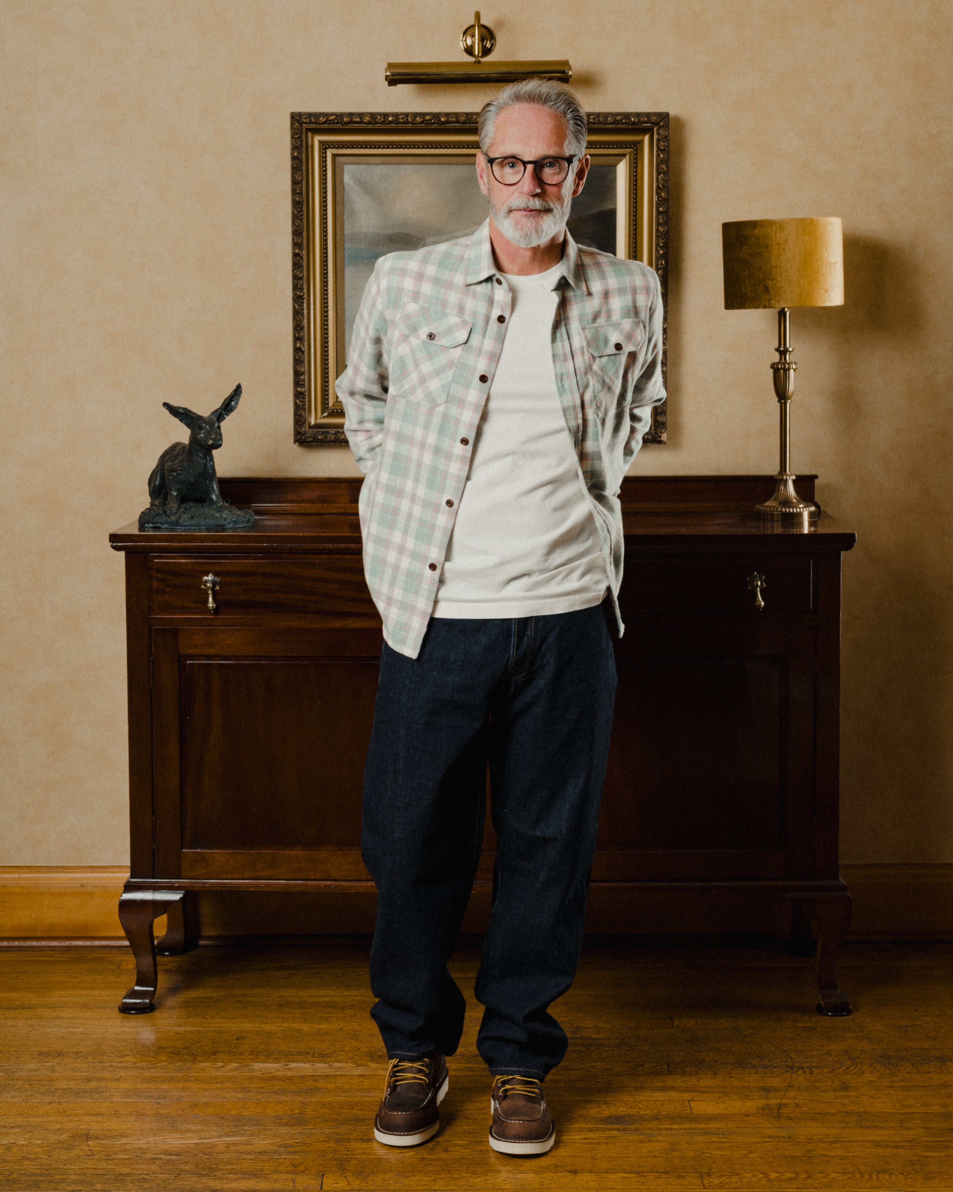 Man standing in a room with a wooden cabinet, lamp, and framed picture in the background.