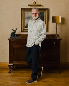Man standing in a room with a painting on the wall and a lamp on a cabinet.