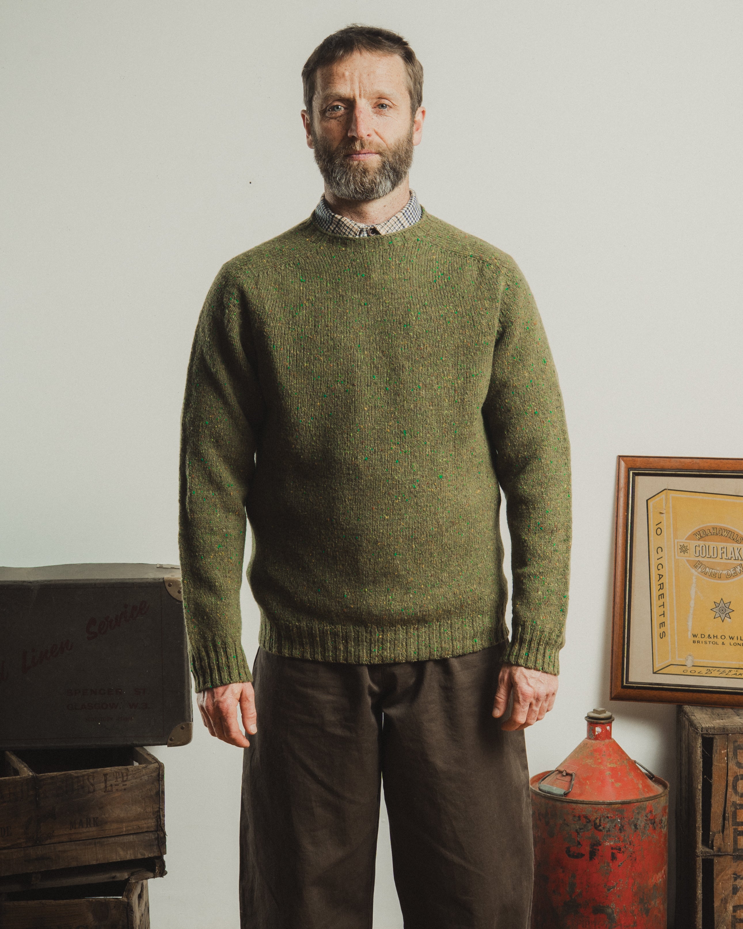 Man wearing a green knitted sweater standing in a room with vintage items.