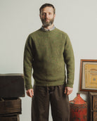 Man wearing a green knitted sweater standing in a room with vintage items.