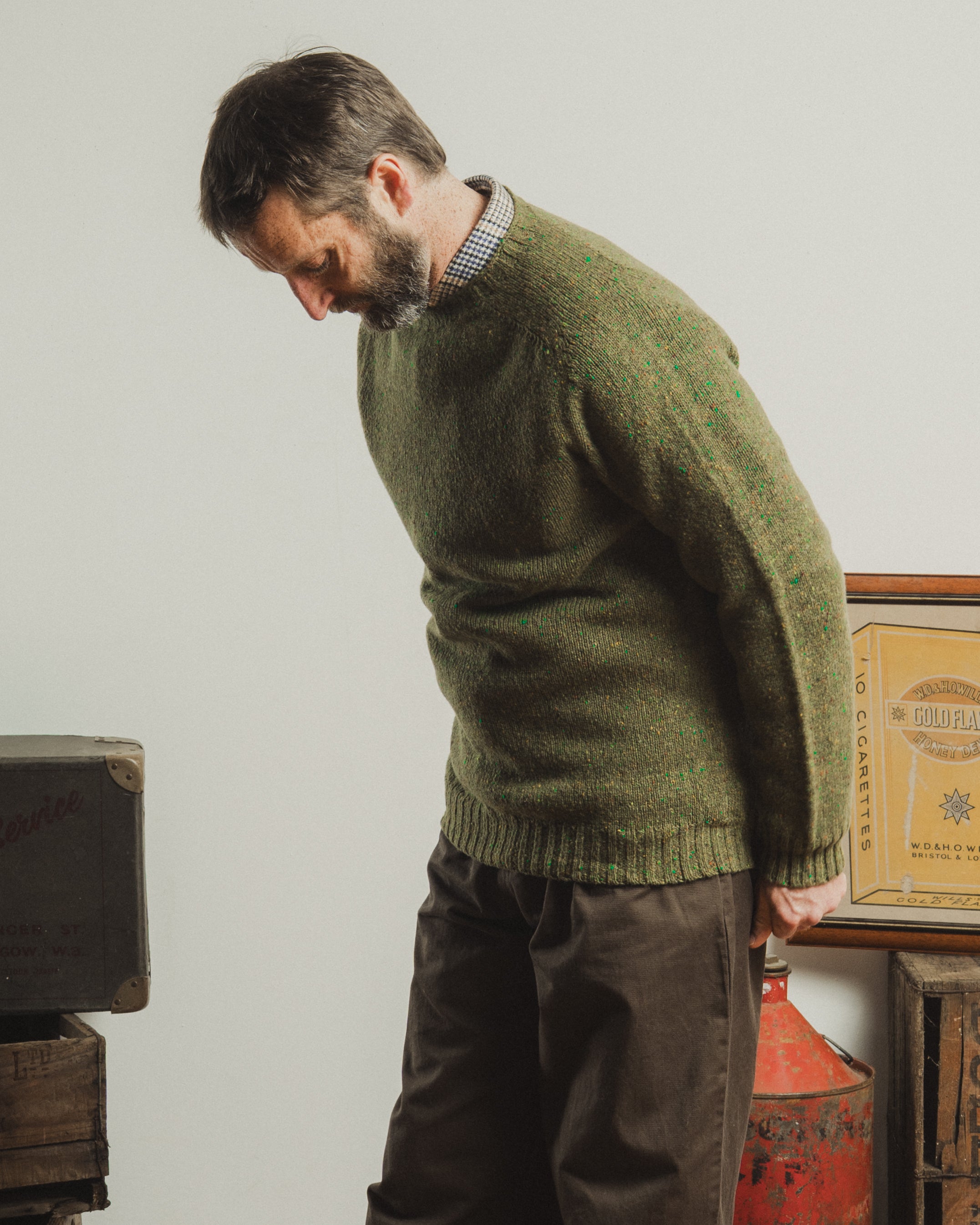 Man wearing a green knitted sweater in a room with vintage boxes.