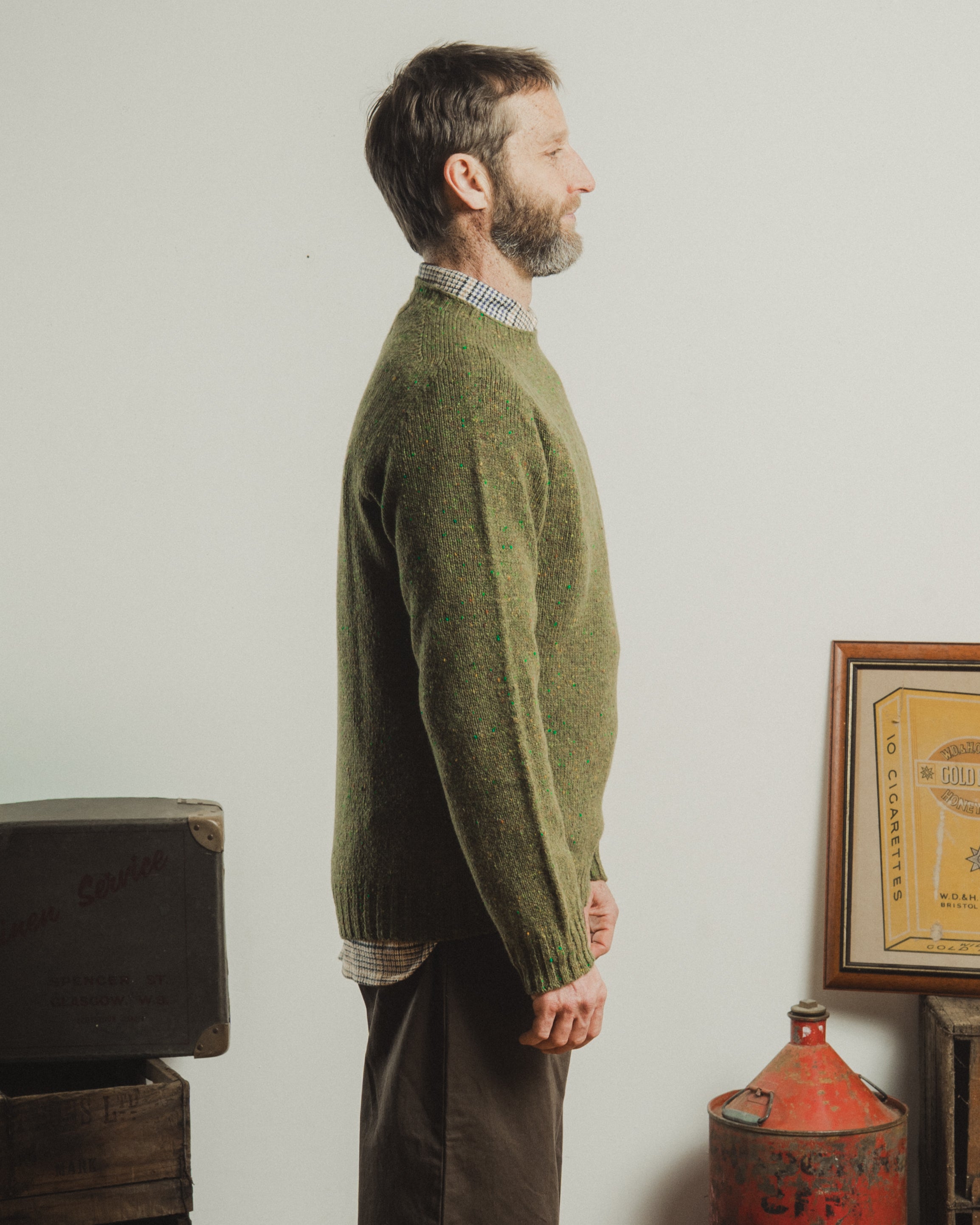 Man wearing a green sweater standing in a room with a white wall and vintage items.