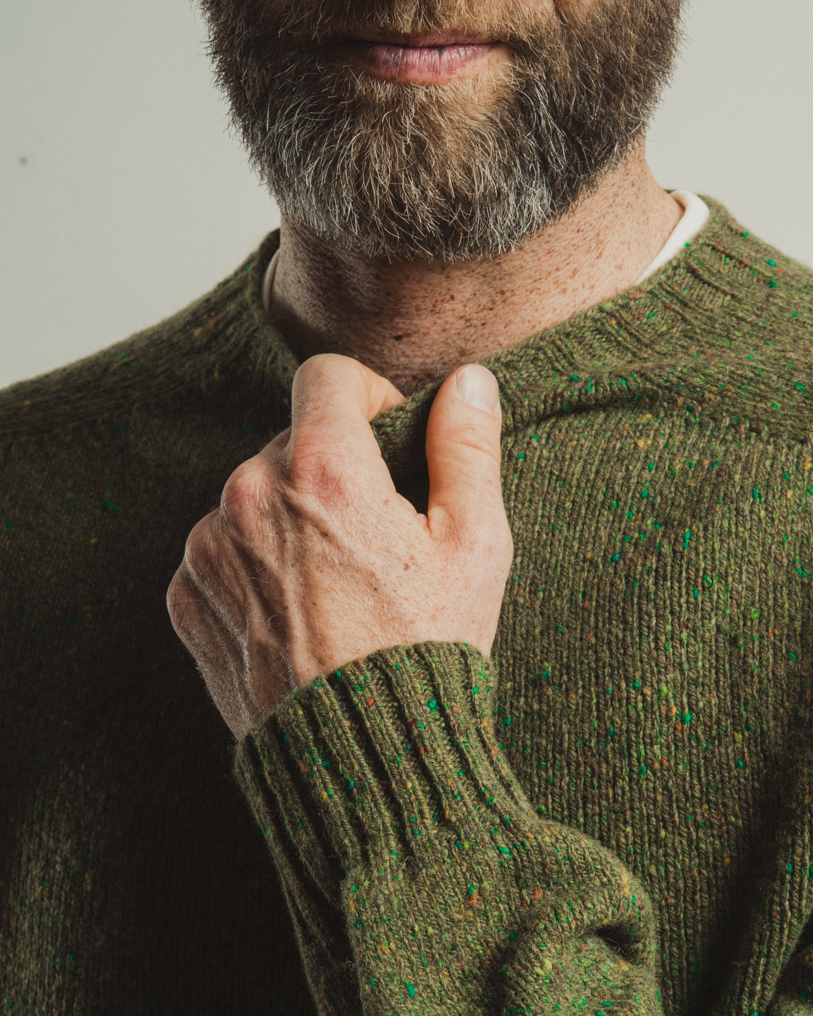 Man wearing a green sweater adjusting his collar against a neutral background