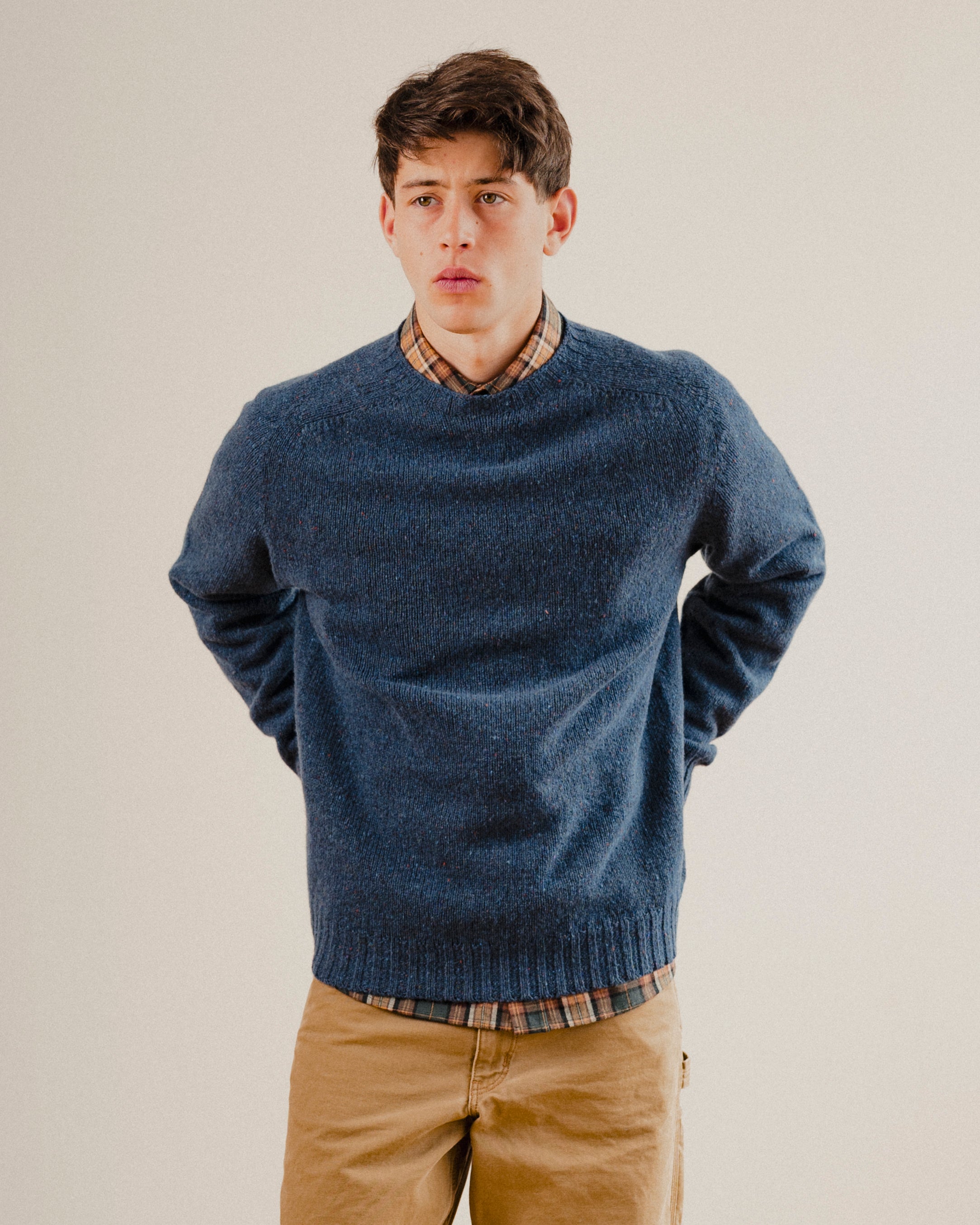 Man wearing a navy blue wool sweater knit crewneck with a check shirt