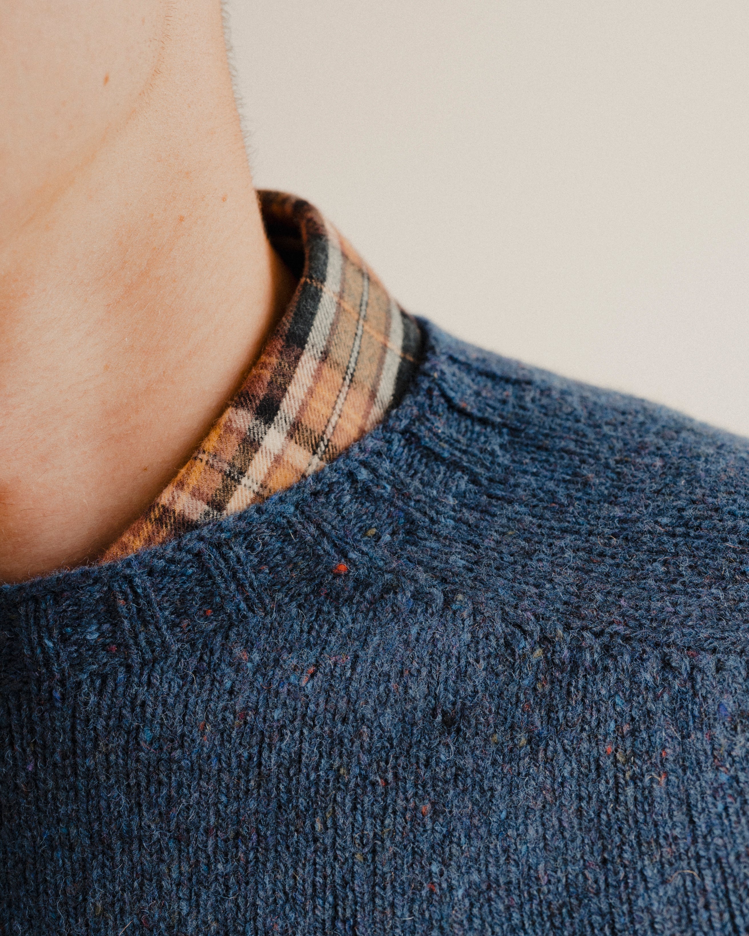 Close up on the neckline of a navy blue wool sweater knit crewneck with a check shirt underneath