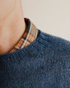 Close up on the neckline of a navy blue wool sweater knit crewneck with a check shirt underneath
