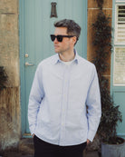 Man wearing a light blue striped shirt standing in front of a teal door.