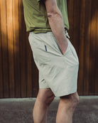 Person wearing light-colored shorts and a green shirt against a wooden wall.