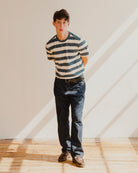 Man wearing a blue and white striped t-shirt and jeans standing in a room with wooden floor and white walls.