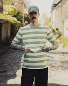 Man wearing a green and white striped shirt and a blue cap with 'Stetson' logo outdoors.