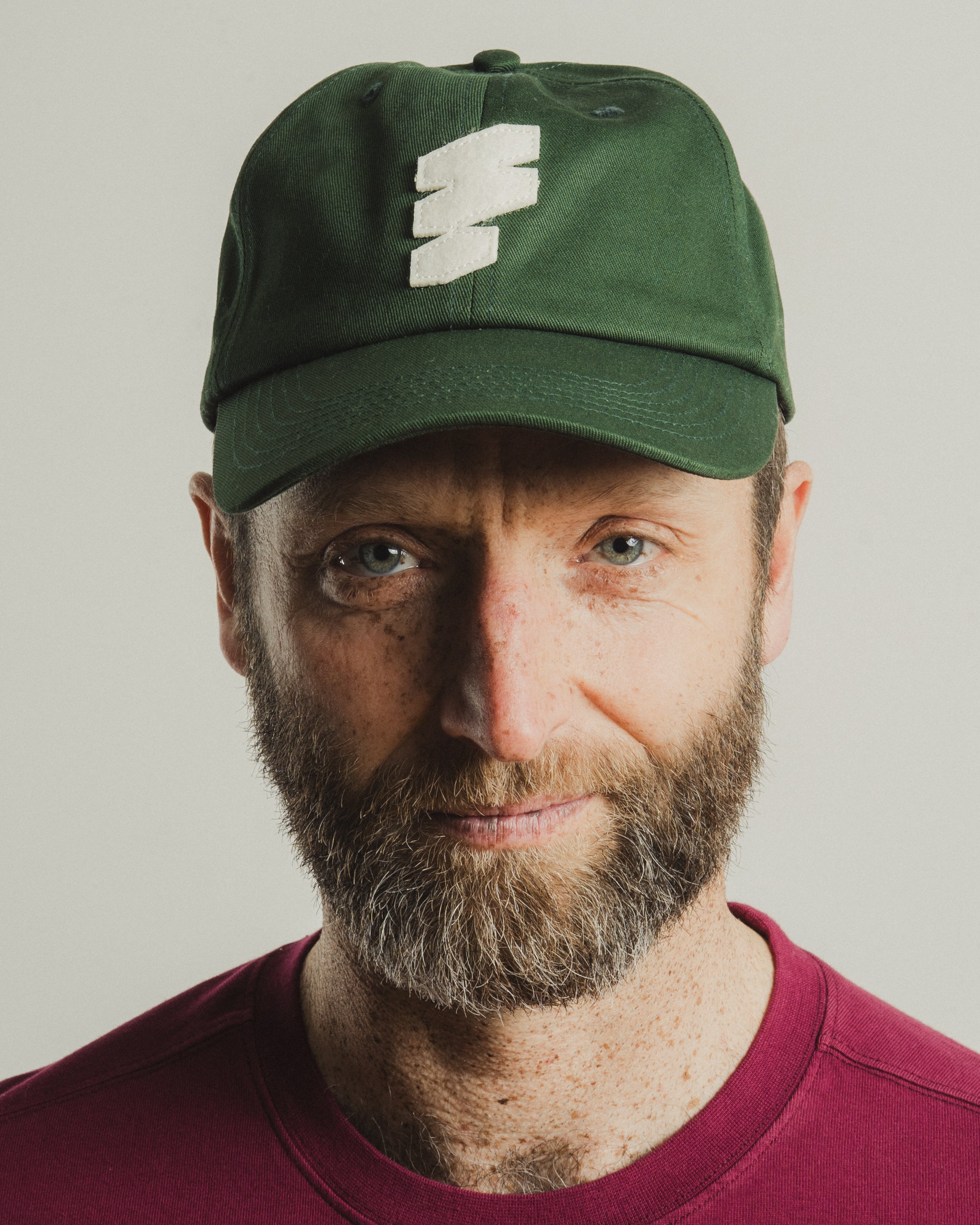 Man wearing a green cap with a logo on a plain background