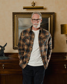 Man wearing a plaid shirt standing in a room with a painting on the wall.