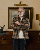 Man wearing a plaid shirt standing in a room with a painting and decorative items on the wall.