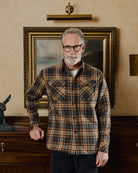 Man wearing a plaid shirt standing in front of a painting on a wall.
