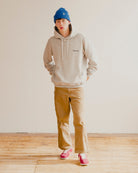 Person wearing a grey hoodie, blue beanie, and tan pants standing in a room with wooden flooring.
