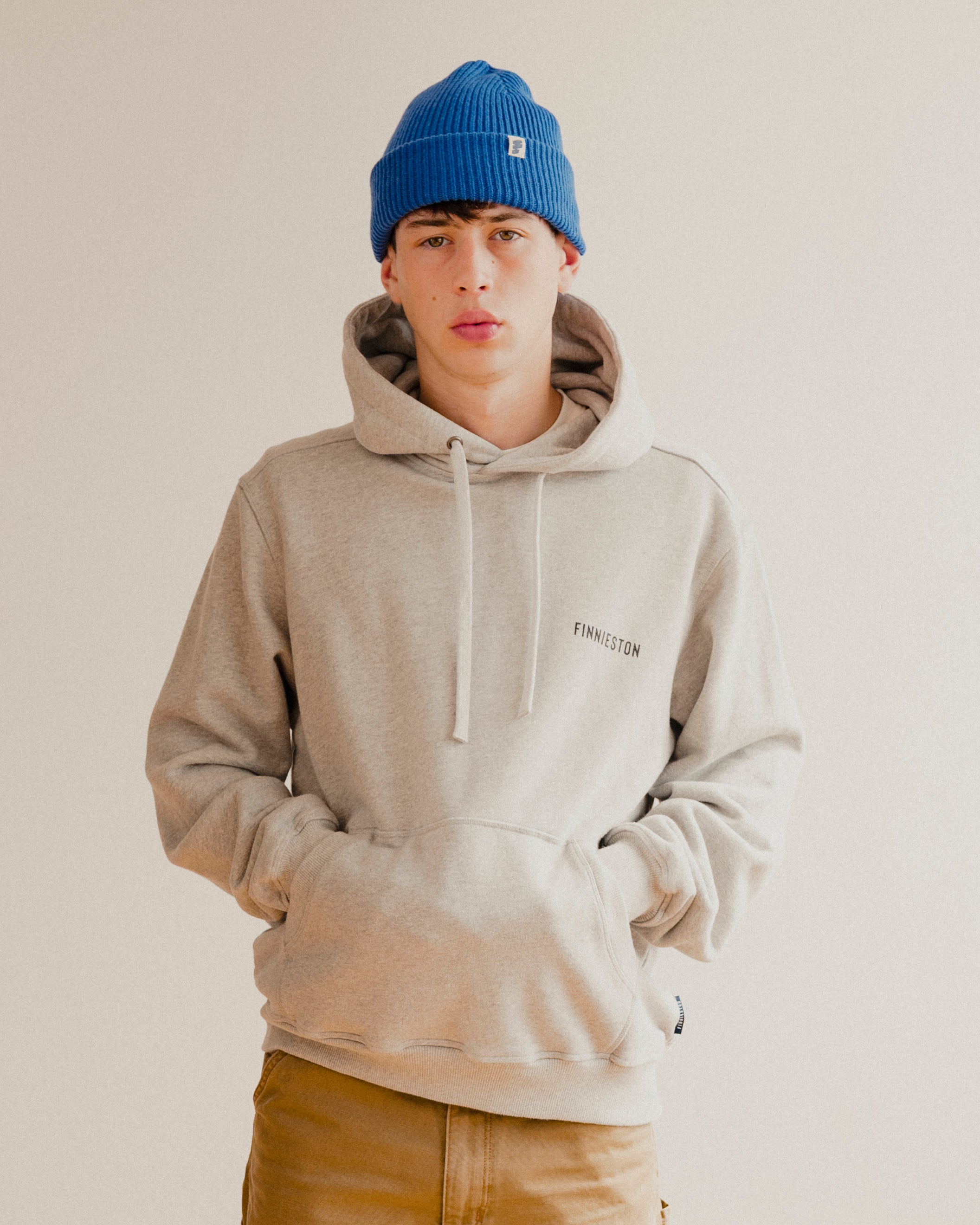 Person wearing a grey hoodie and blue beanie on a plain background