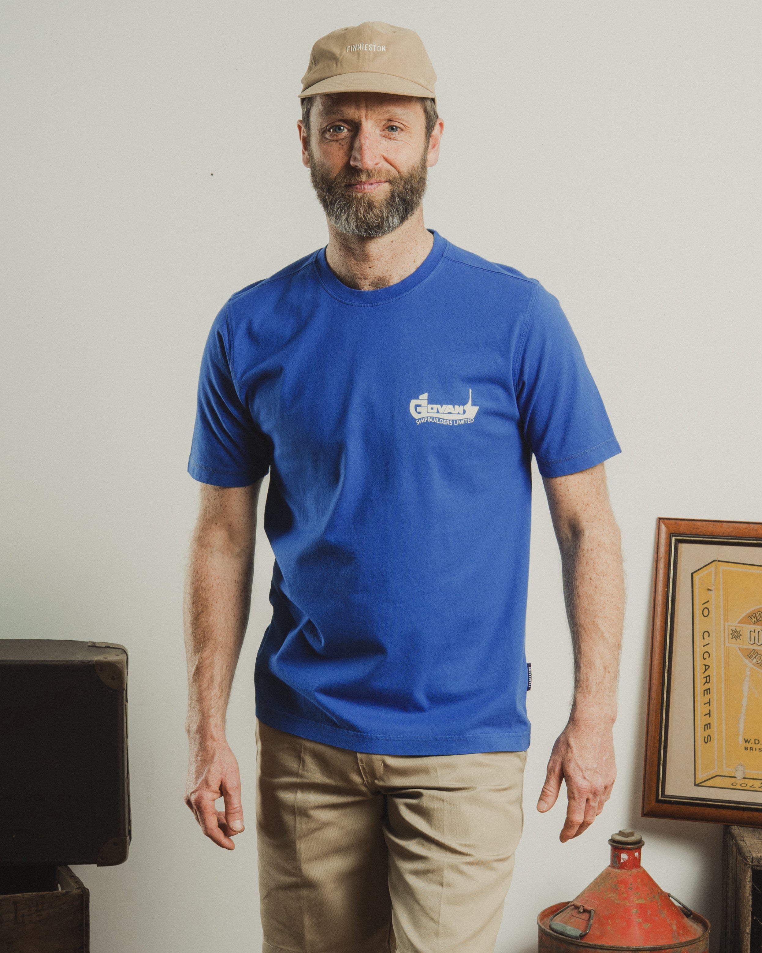 Man wearing a blue t-shirt with a logo, standing indoors against a plain wall.