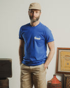 Man wearing a blue t-shirt with a logo, standing in a room with vintage items.