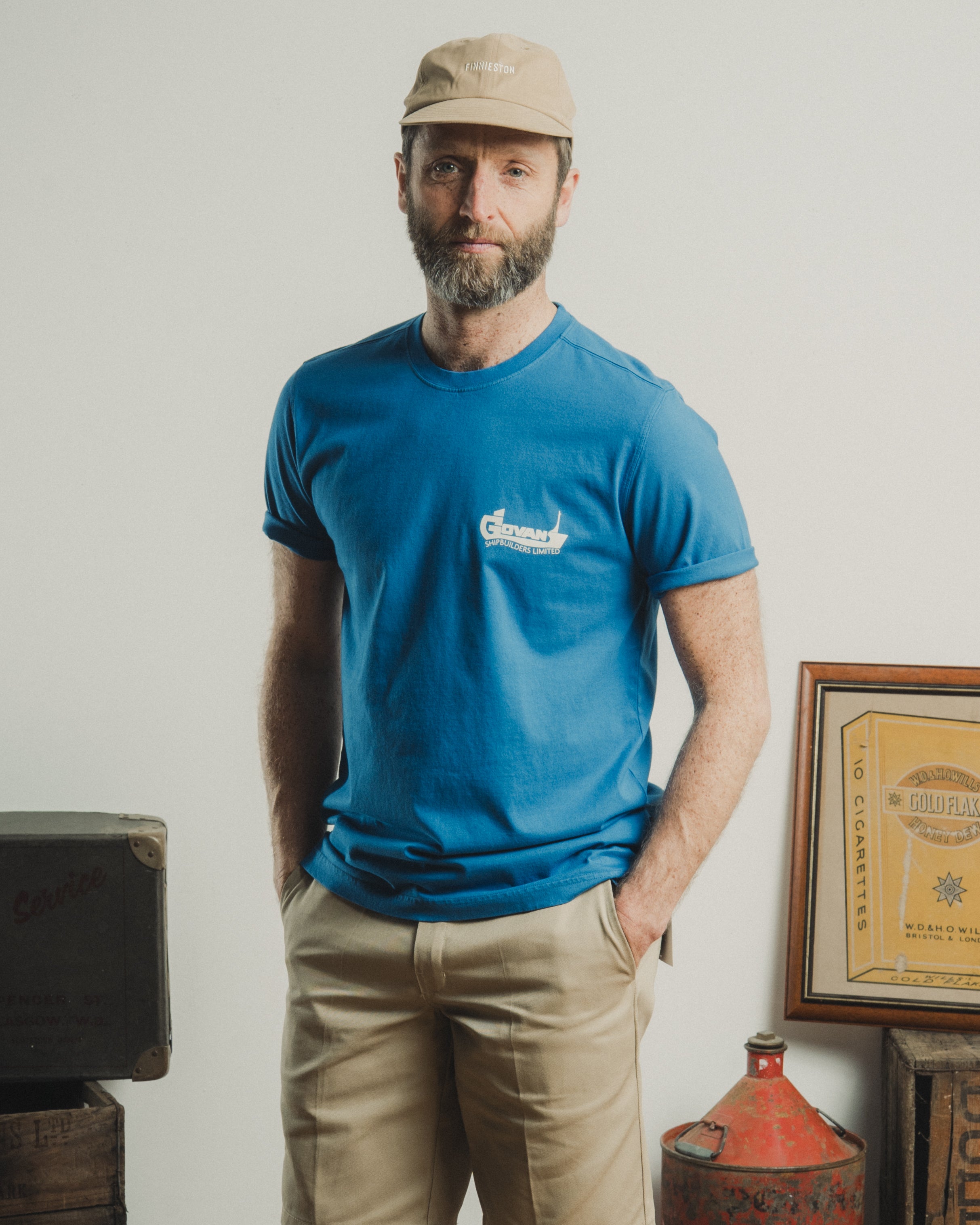 Man wearing a blue t-shirt with a logo, standing in a room with vintage items.