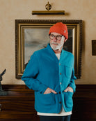 Man wearing a blue jacket and orange beanie standing in front of a painting