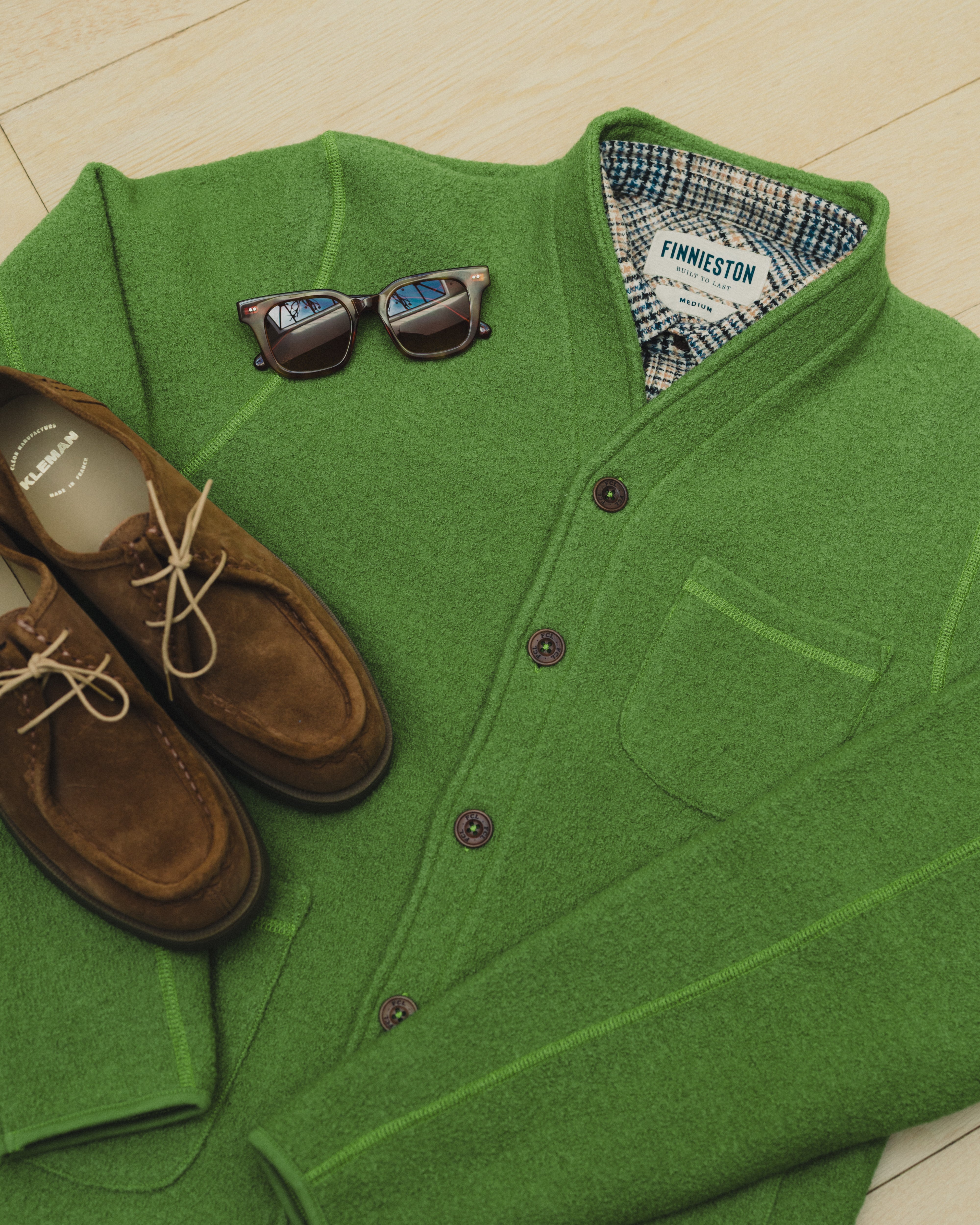 Green cardigan with sunglasses and brown shoes on a light background