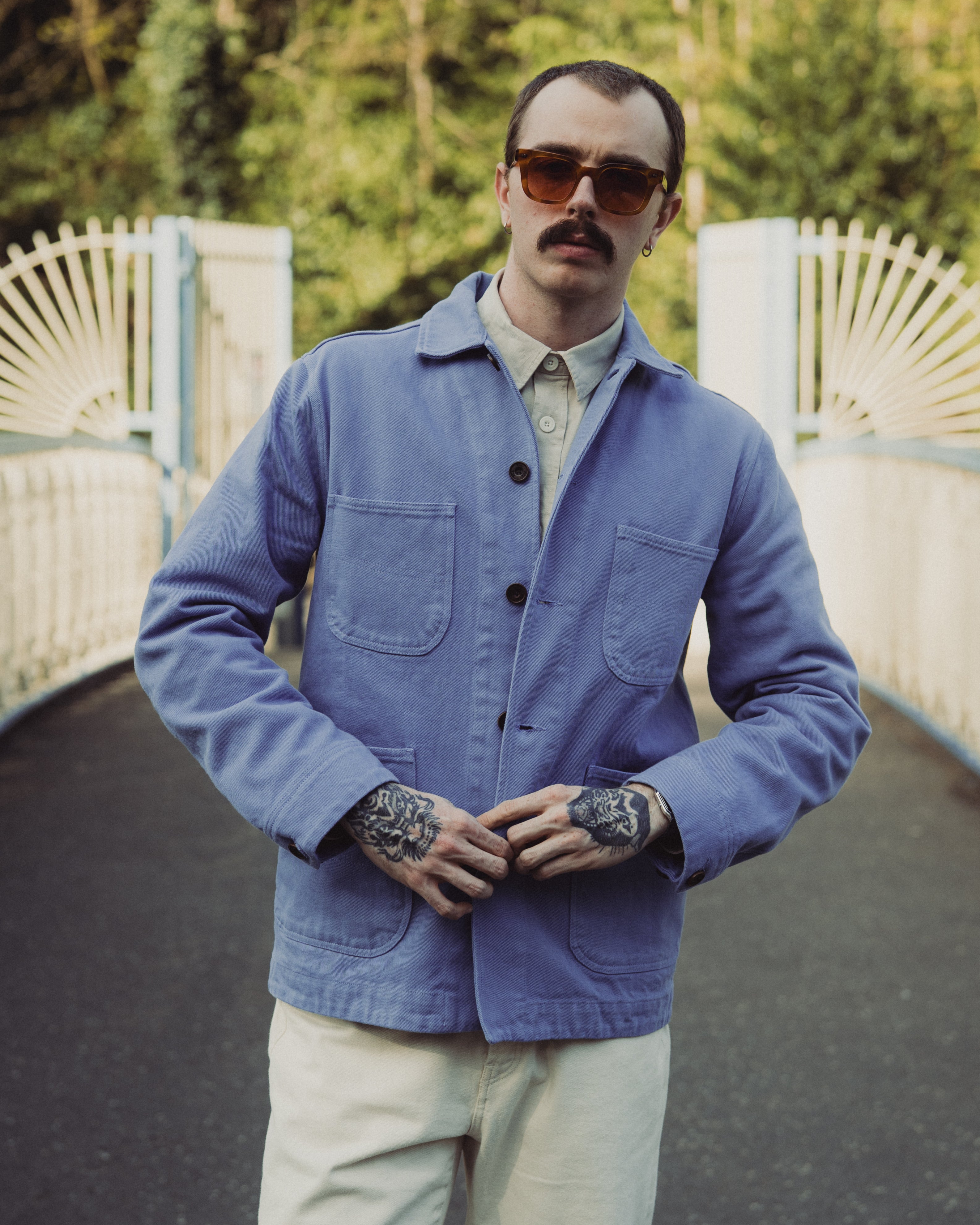 Man wearing a blue jacket and sunglasses standing outdoors with a blurred background