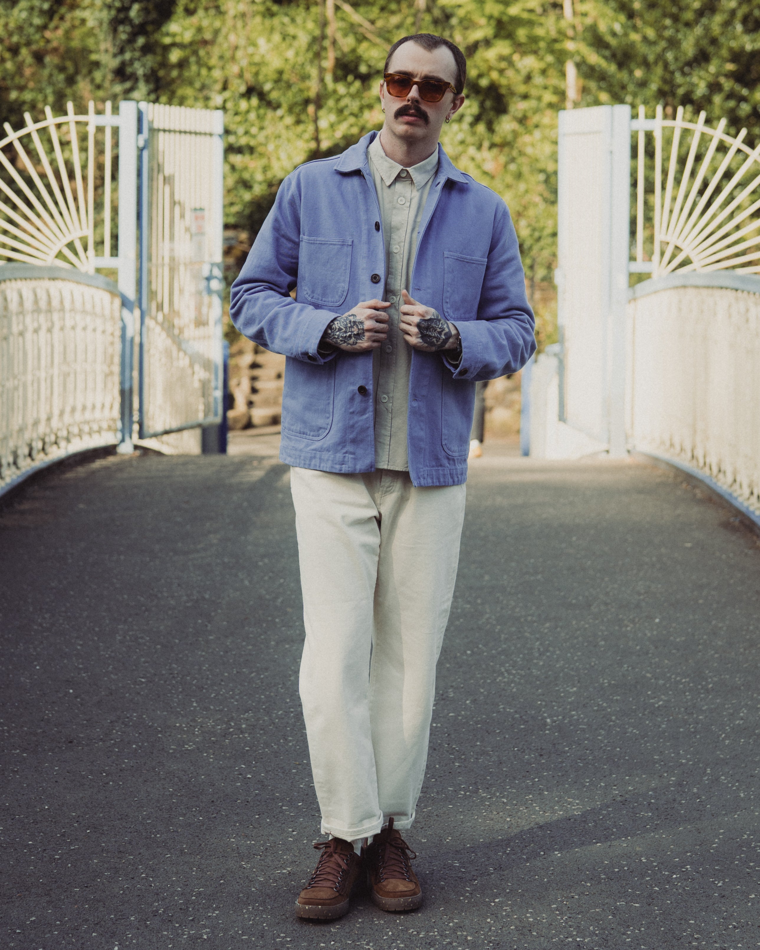 Man wearing a blue jacket and sunglasses standing on a bridge
