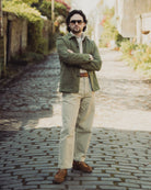 Man standing on a cobblestone street wearing a green jacket and sunglasses.